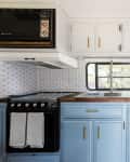 Camper kitchen with blue cabinets, wood countertops, sunflower in vase, and patterned backsplash.