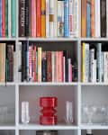 Bookshelf with assorted books, red vase, and glassware on lower shelves.