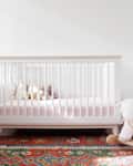 Nursery with a white crib, stuffed animals, colorful rug, dresser, and a plush rocking sheep.
