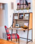 Home office with a wooden desk, red striped chair, framed photos, and potted plants on top.