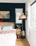 Bedroom with a rustic wooden headboard, vintage lamp, and a tree stump nightstand with books and a plant.