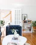 Living room with blue velvet sofas, white coffee table, plants, bookshelf, and staircase in the background.