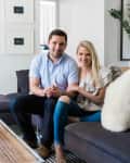 Couple sitting on a gray sofa in a modern living room with framed art and a striped rug.