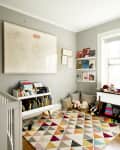 Nursery with gray walls, colorful geometric rug, crib, bookshelves, toys, and framed duck artwork.