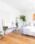 Bright bedroom with wooden floor, potted plants, a cozy bed, and wall art.