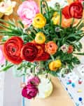 Colorful ranunculus bouquet in a vase on a table next to a book titled "Beaches."