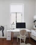 Home office with white desk, computer, armchair, potted plant, and framed artwork on wooden floor.