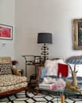 Eclectic living room with a blue tufted sofa, vintage artwork, patterned armchair, and decorative lamps on side tables.