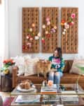 Woman sitting on a brown leather sofa with a cat, surrounded by colorful decor and bookshelves in a cozy living room.