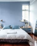 Bedroom with blue accent wall, double bed, blue pillows, wooden nightstands, and a large window.