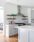 Modern kitchen with white countertops, stainless steel appliances, open shelves, and pink flowers on the counter.