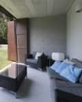 Covered patio with wicker furniture, blue cushions, glass table, and view of a grassy yard with a pool and trees.