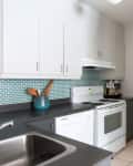 Modern kitchen with white cabinets, teal backsplash, and shelves of glass jars filled with spices and ingredients.