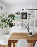 Dining room with wooden table, white chairs, large plant, and gallery wall of colorful framed art.