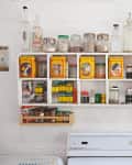 Kitchen shelves with vintage tins, glass jars, spices, and dishes above a white stove.