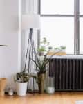 Living room corner with potted plants, a black radiator, and a tall floor lamp by a large window.
