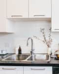 Modern kitchen with black countertop, stainless steel sink, fruit bowl, espresso maker, and white cabinets.