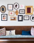 Wooden bench with floral cushions and a DC pillow, beneath a gallery wall of framed art and silhouettes.