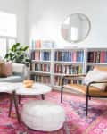 Living room with light blue sofa, colorful pillows, pink rug, round coffee tables, bookshelves, and cactus artwork.