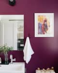 Bathroom with purple accent wall, large mirror, white sink, towel, and colorful artwork.