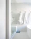 Modern bathroom with glass shower, white towels on hooks, and light wood vanity.