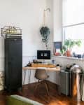 Home office with wooden desk, computer, plants, vintage decor, and a black cabinet on wooden floor.