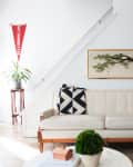 Mid-century modern living room with a cream sofa, geometric pillow, potted plant, and framed tree artwork.