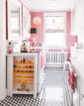 Pink kitchen with patterned floor, white cabinets, colorful decor, and a window with floral blinds.