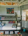 Bunk bed with colorful bedding, a wall tapestry, and toys in a cozy, light-filled room.