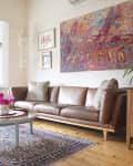 Living room with brown leather sofa, colorful abstract art, wooden furniture, and a patterned rug.