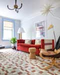 Living room with red sofa, patterned rug, leather lounge chair, and large windows with blue trim.