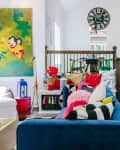 Colorful living room with a blue sofa, vibrant pillows, abstract art, and a large clock on the wall.