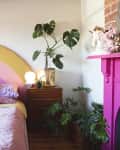 Bedroom with rainbow headboard, pink quilt, colorful pillows, plants, and a pink fireplace with unicorn decor.