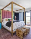 Canopy bed with pink headboard, blue nightstand, leopard print stools, and tropical wallpaper in a bright bedroom.
