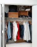 Organized closet with hanging clothes, wooden crates, bags, and a white dresser.