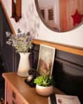 Cat sitting on dark staircase in hallway with patterned tile floor, wooden door, round mirror, and decorative plants.
