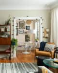 Cozy living room with a mustard door, wooden shelf, plants, and a view into a dining area with a round table and white chairs.