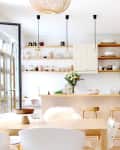 Bright kitchen with wooden dining table, pendant lights, open shelves, and white cabinets.