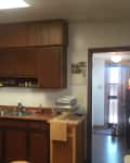 Dated kitchen with dark wood cabinets, double sink, and gas stove, leading to a hallway with a door.