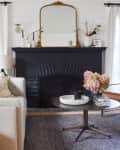 Living room with beige sofa, black fireplace, round coffee table, and leather chair, featuring floral arrangement and decor.
