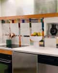 Kitchen with colorful tiled backsplash, fruit bowl, black pitcher, and stacked pastel cups on a white countertop.