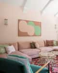 Living room with pink sectional sofa, abstract wall art, colorful rug, green armchair, and bookshelves by a large window.