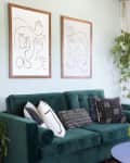 Green velvet sofa with patterned cushions, abstract line art, and hanging plants in a bright living room.