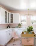 Pink kitchen with white cabinets, gas stove, potted plants, and a wooden table with pink chairs.