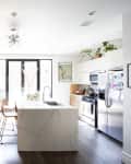 Bright kitchen with marble island, wooden floors, plants, and modern appliances.