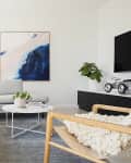 Modern living room with a light gray sectional sofa, abstract blue artwork, and a round coffee table with plants.