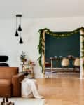 Mid-century living room with brown leather sofa, holiday decor, and view into dining room with green wall and garland.