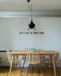 Dining room with wooden table, wicker chairs, black pendant light, and wall text "Let's go to New York."