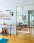 Living room with orange curtains, armchair, geometric pillow, blue rug, and console table with vase and decor.