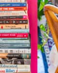 Stack of colorful books on a pink shelf next to a wooden chair and green plant.